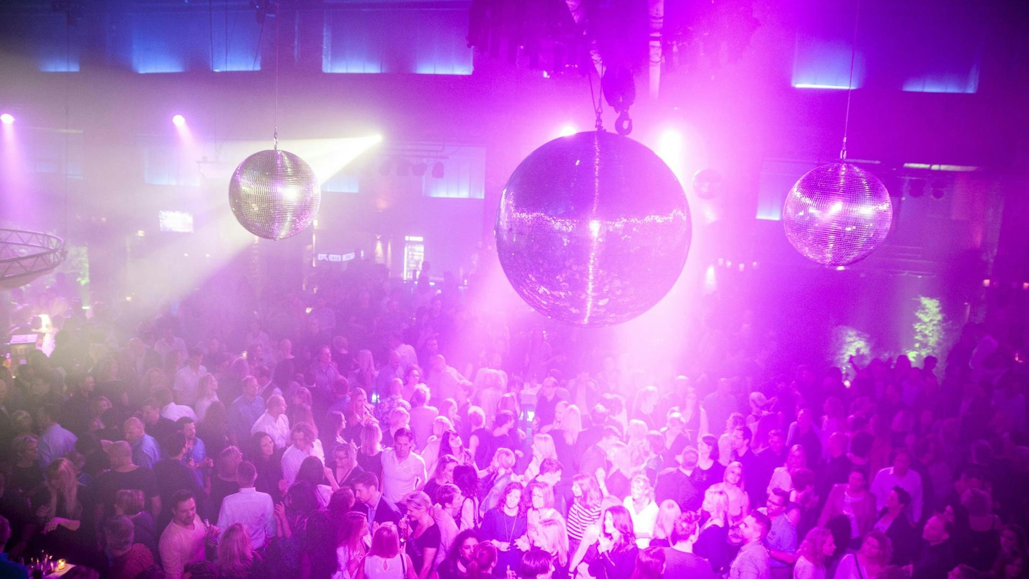 Menschen tummeln sich auf der Tanzfläche in der Halle Tor 2, sie werden von Disco-Kugeln angestrahlt.