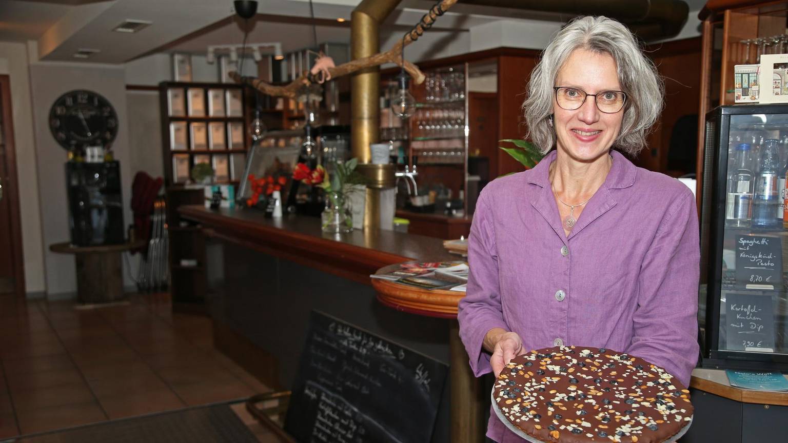 Elke Kremer steht in ihrem Café und hät einen Schokoladenkuchen in der Hand.
