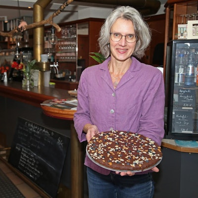 Elke Kremer steht in ihrem Café und hät einen Schokoladenkuchen in der Hand.