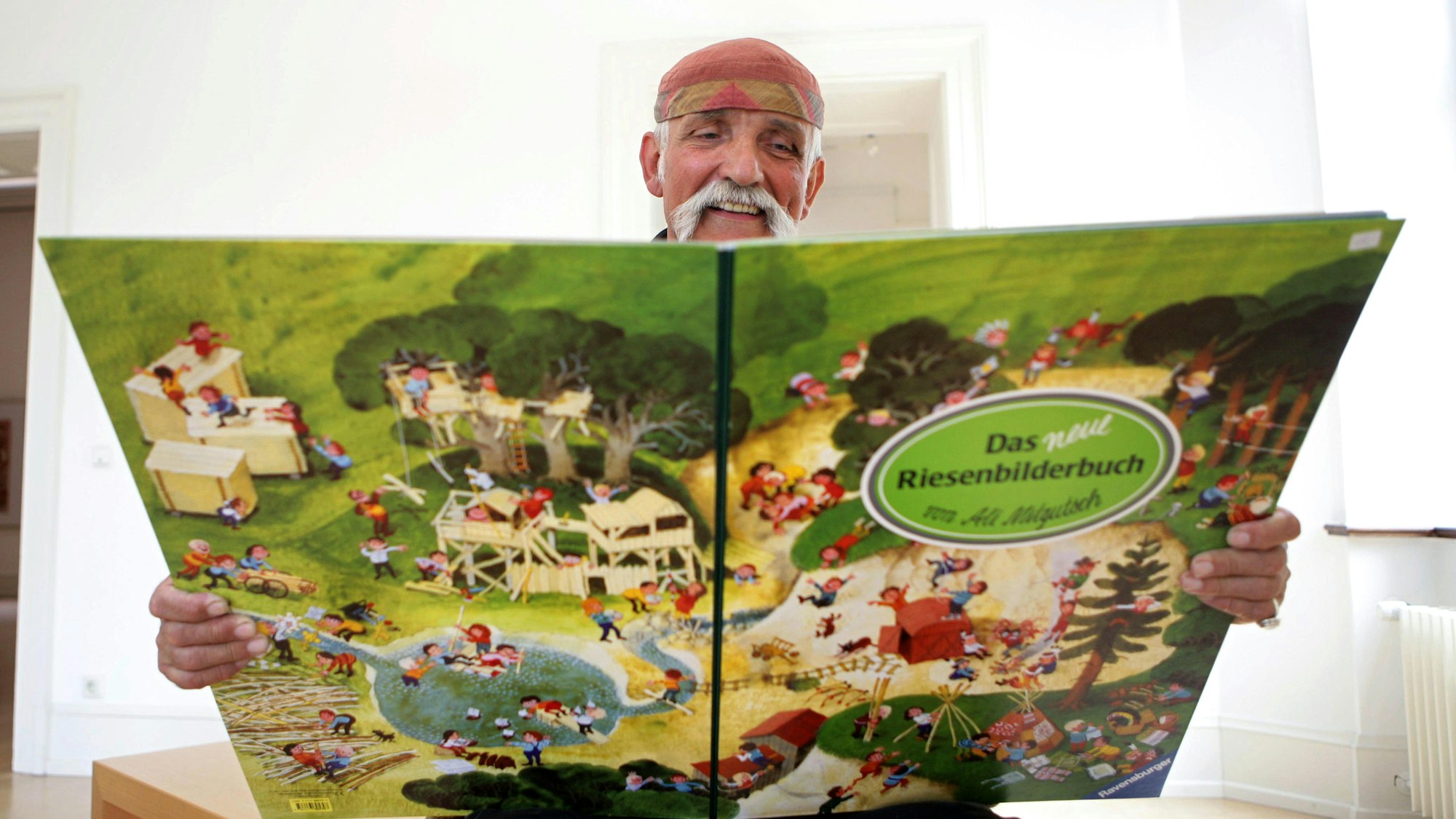 Mann mit Kopfbedeckung und weißem Schnauzbart hält ein großes Bilderbuch in den Händen