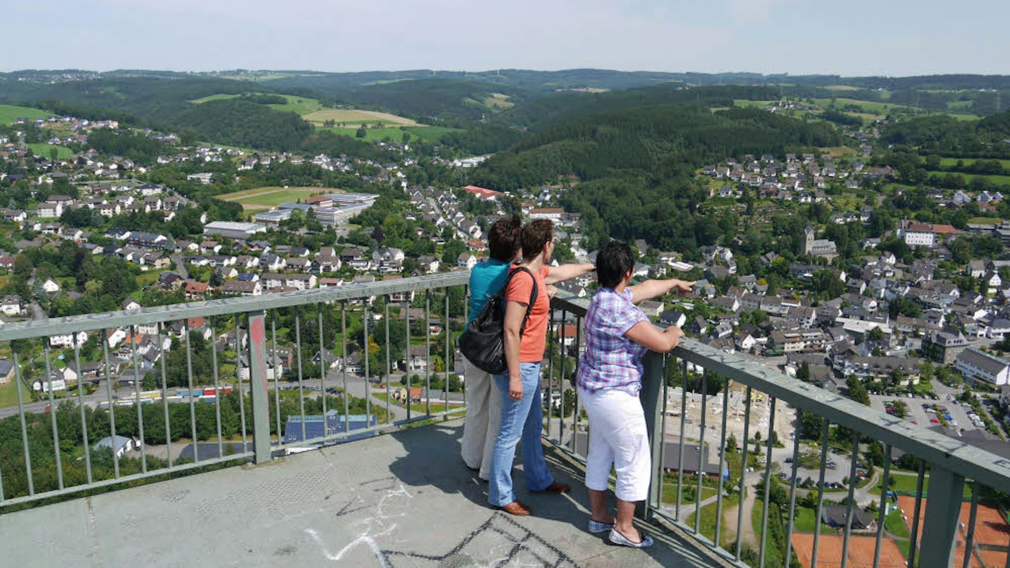 Menschen stehen auf einem Aussichtspunkt und schauen in ein Tal.