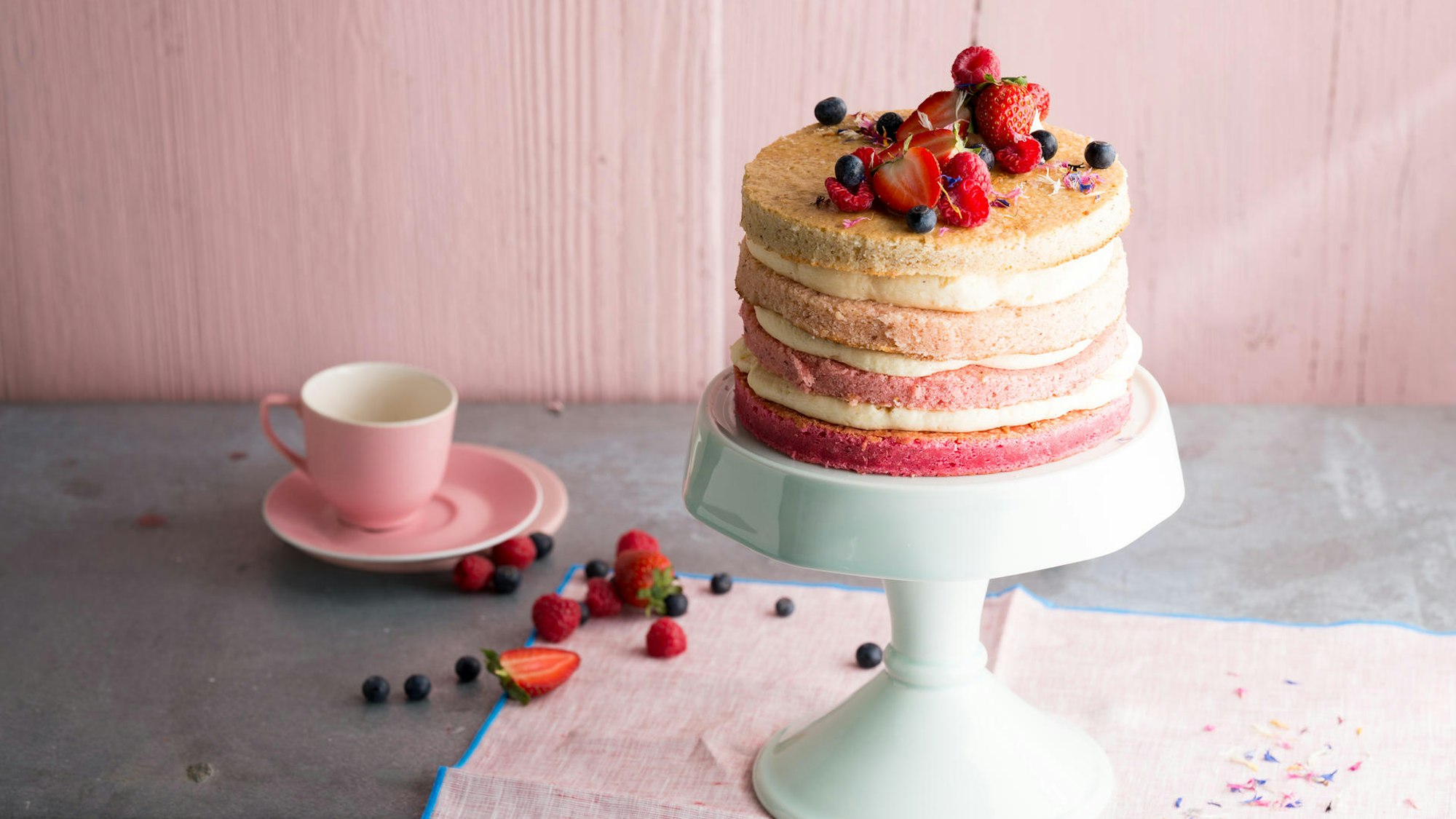 Eine schöne, zartrosa Torte mit leckeren Schichten wird auf einem Tortenteller präsentiert.