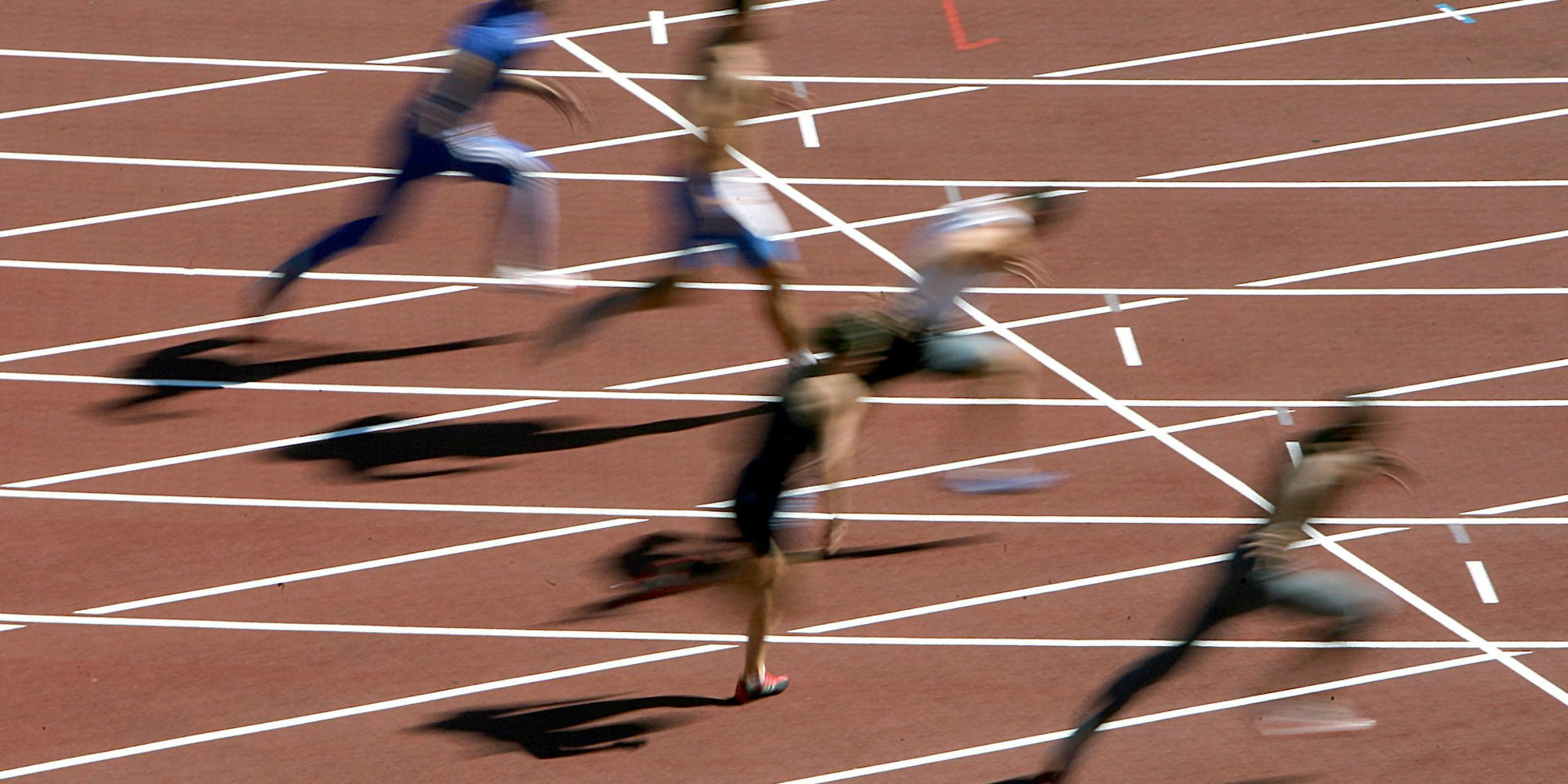 Mehrere Menschen rennen und verschwimmen dabei auf einem typisch roten Feld.