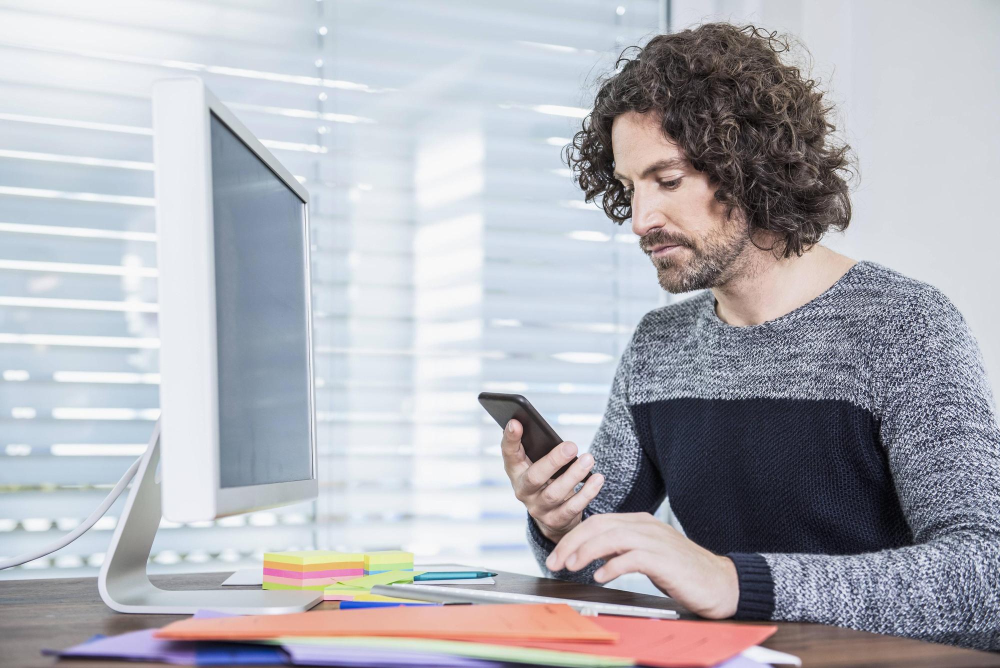 Mann mit Smartphone vor PC