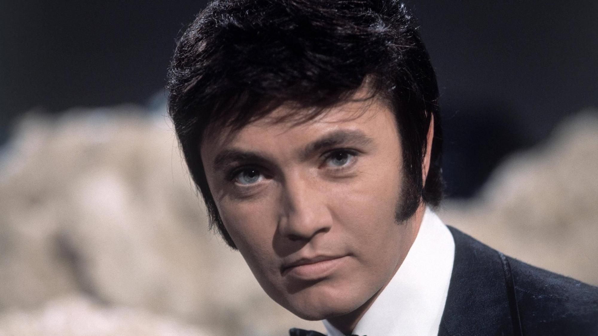 Schlagerstar Rex Gildo bei einem Auftritt in einer Fernsehshow um 1969. Er schaut neutral in die Kamera.