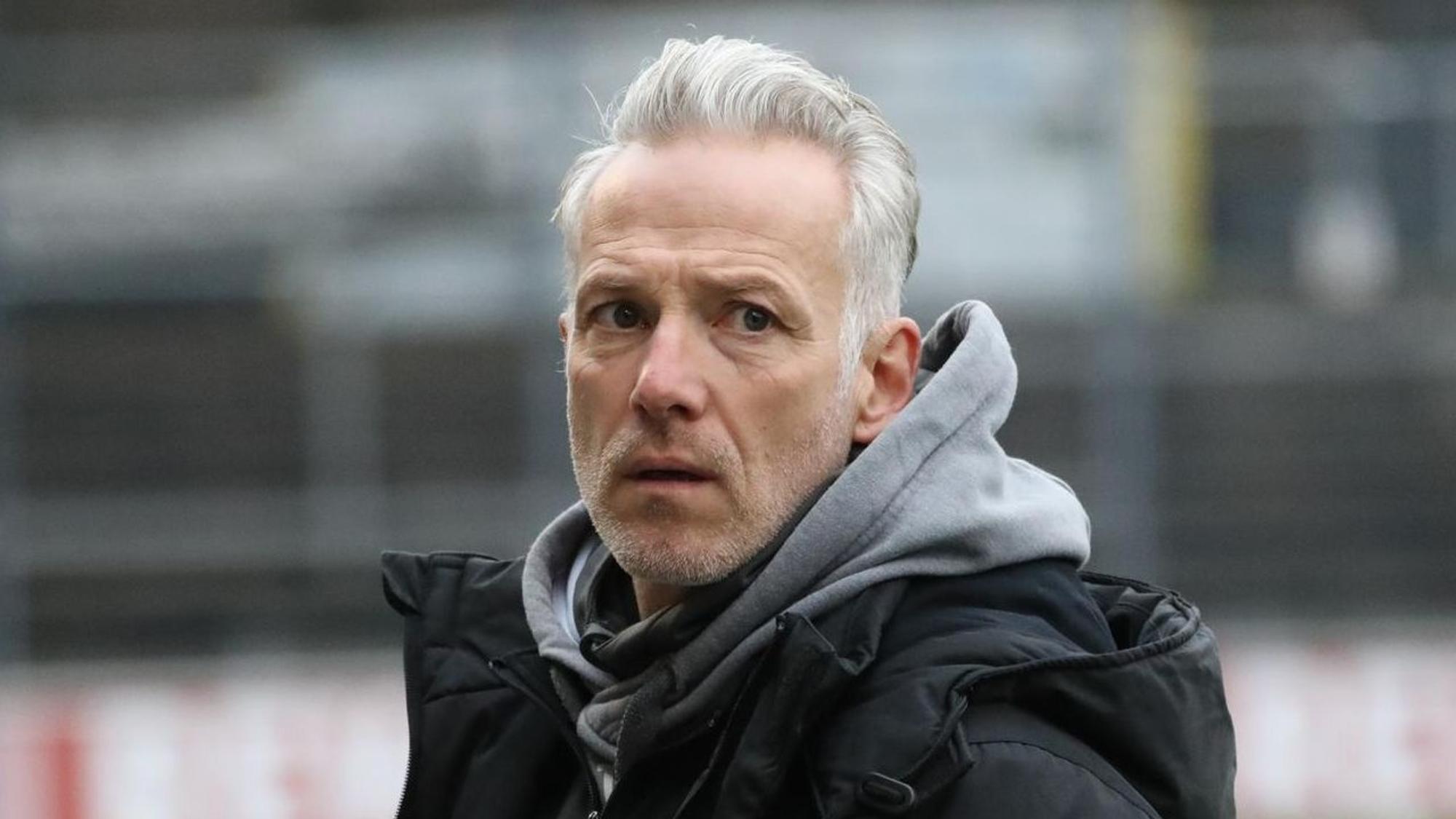 Ein Trainer steht am Spielfeldrand und blickt auf den Platz.
