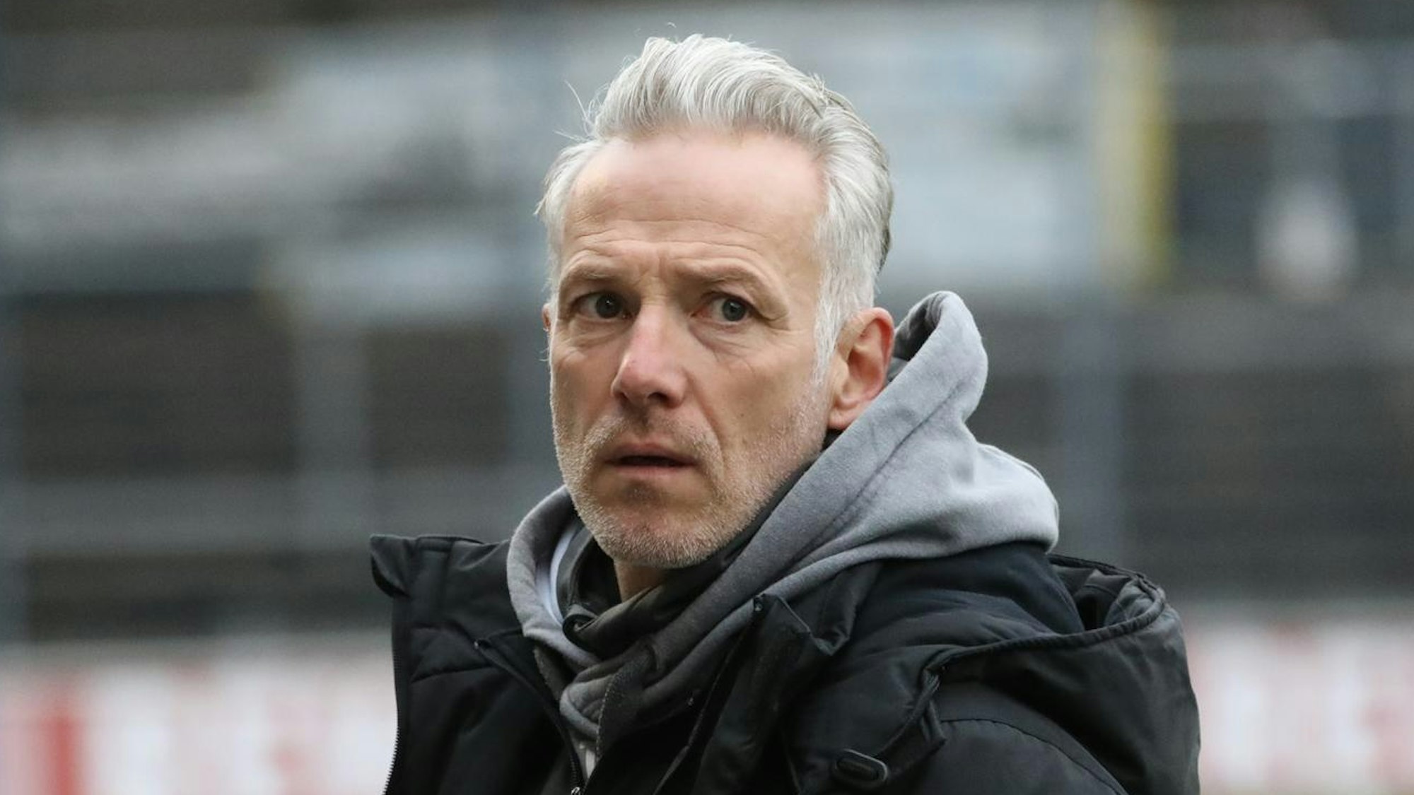 Ein Trainer steht am Spielfeldrand und blickt auf den Platz.