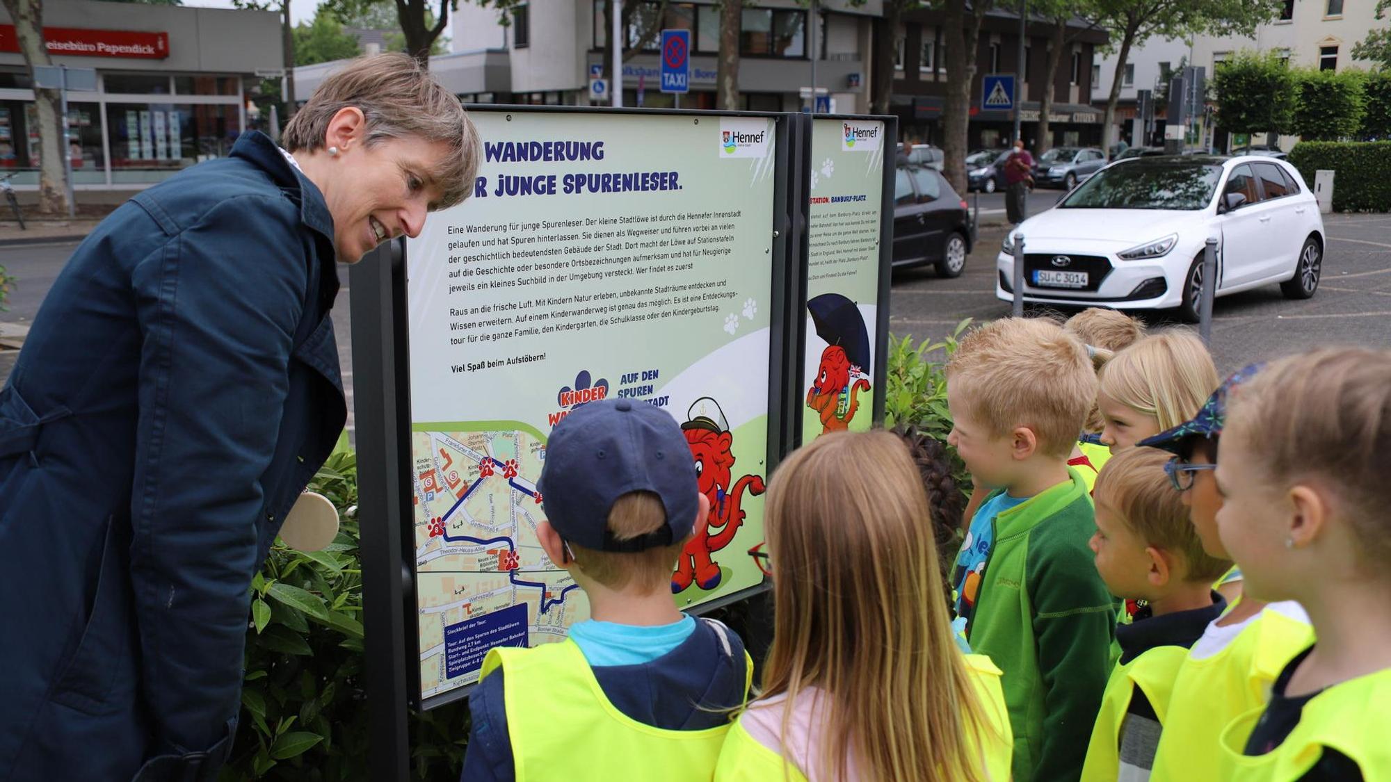 Tina-Viola Oppermann vom Amt für Tourismus steht mit einer Gruppe Kindern vor einem Plan und erklärt ihnen die Wanderwege.
