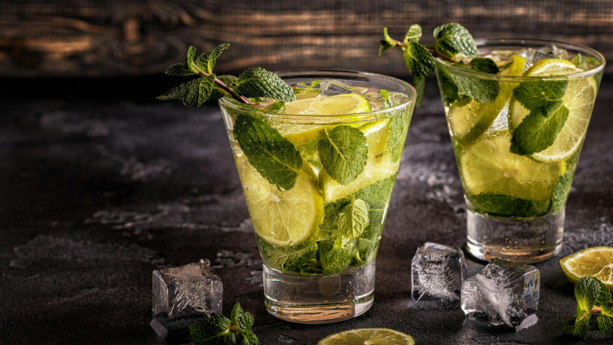 Zwei Cocktailgläser mit Limetten und Minze.