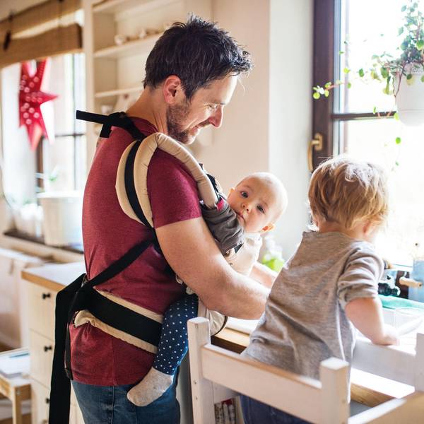 Ein Mann hat ein Baby in der Trage und spült ab.