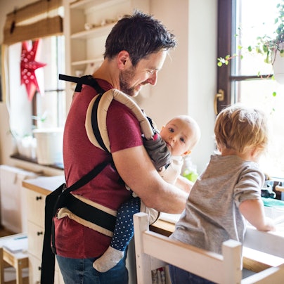Ein Mann hat ein Baby in der Trage und spült ab.
