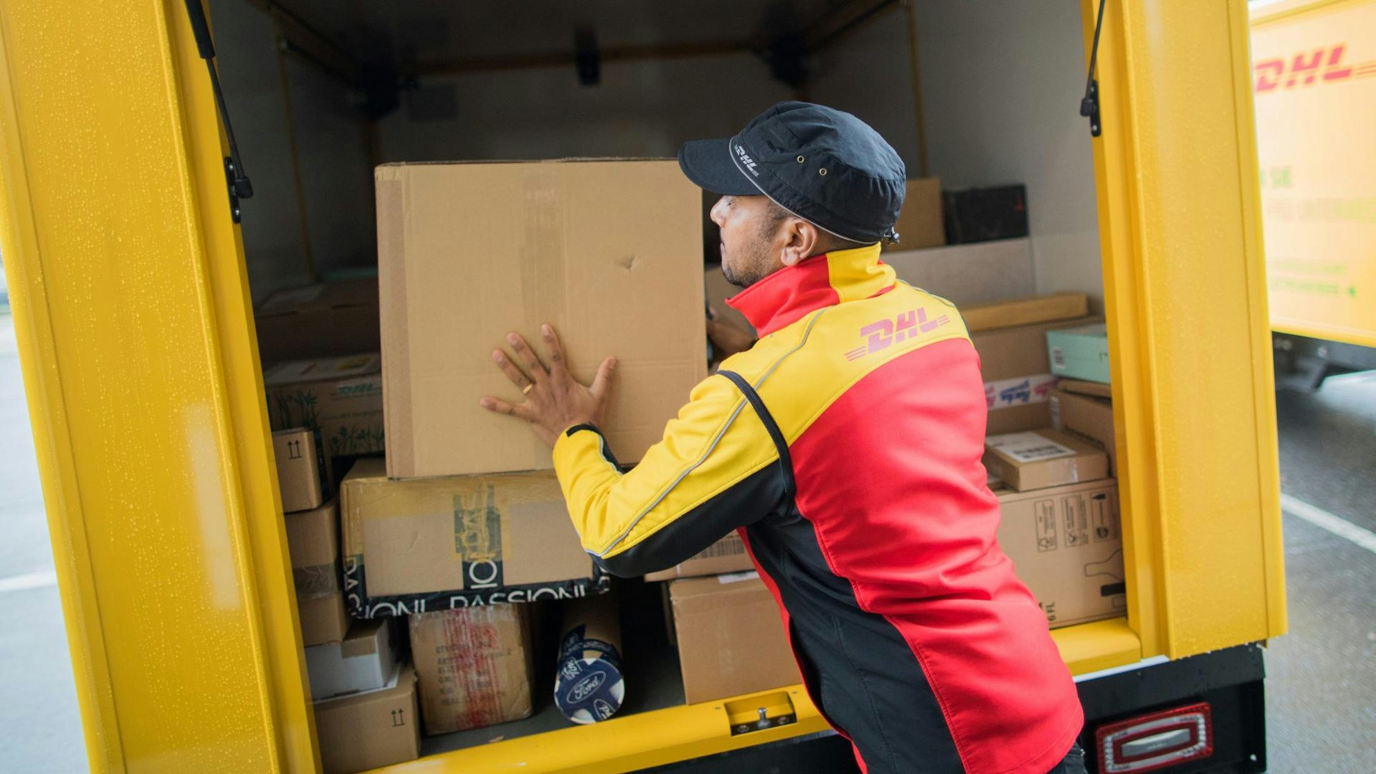 DHL-Paketzusteller lädt Pakete aus einem Auto aus