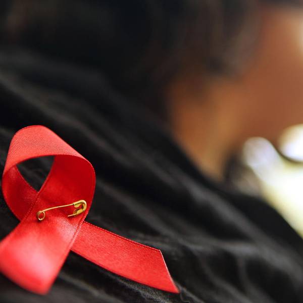 Eine Frau hat sich eine rote Aids-Schleife angesteckt