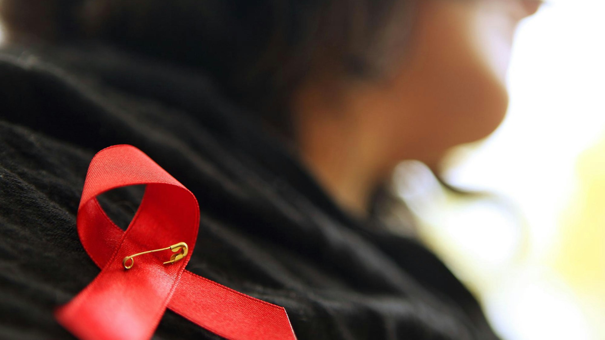 Eine Frau hat sich eine rote Aids-Schleife angesteckt