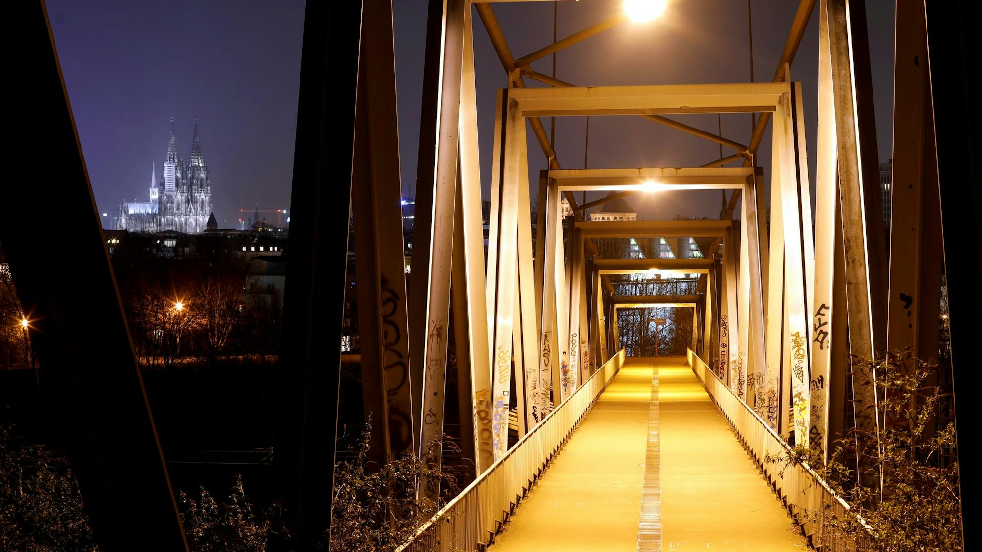 Der Weg der beleuchteten Brücke am Herkulesberg bei Nacht, im Hintergrund ist der Kölner Dom zu sehen.