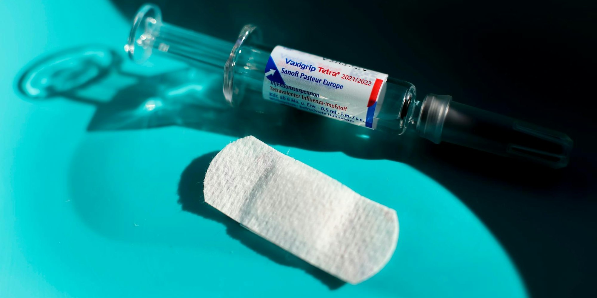 Eine Spritze und ein Pflaster liegen auf einem Tisch bereit.