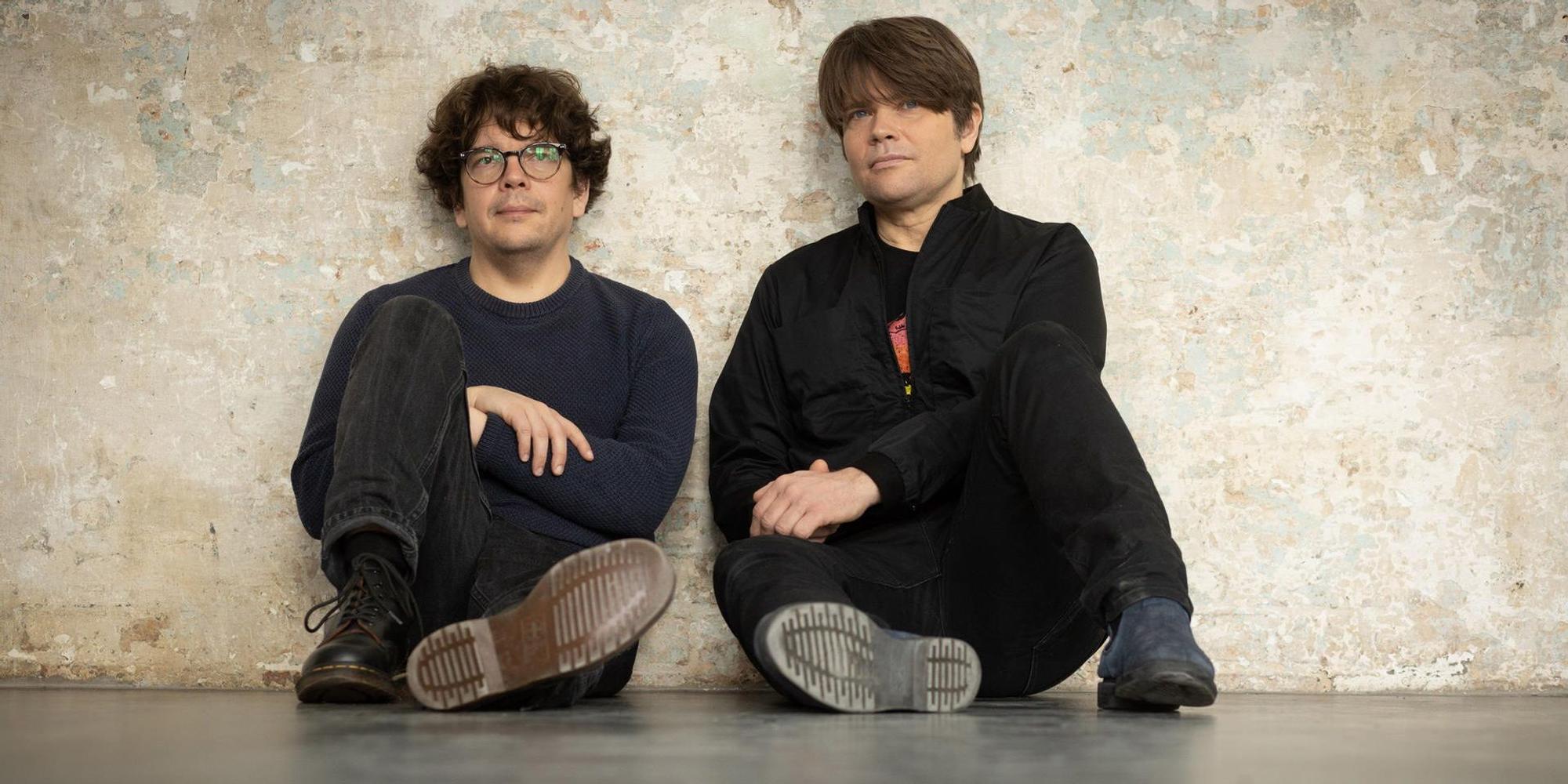 Rasmus Engler und Jan Müller sitzen vor einer Betonwand.