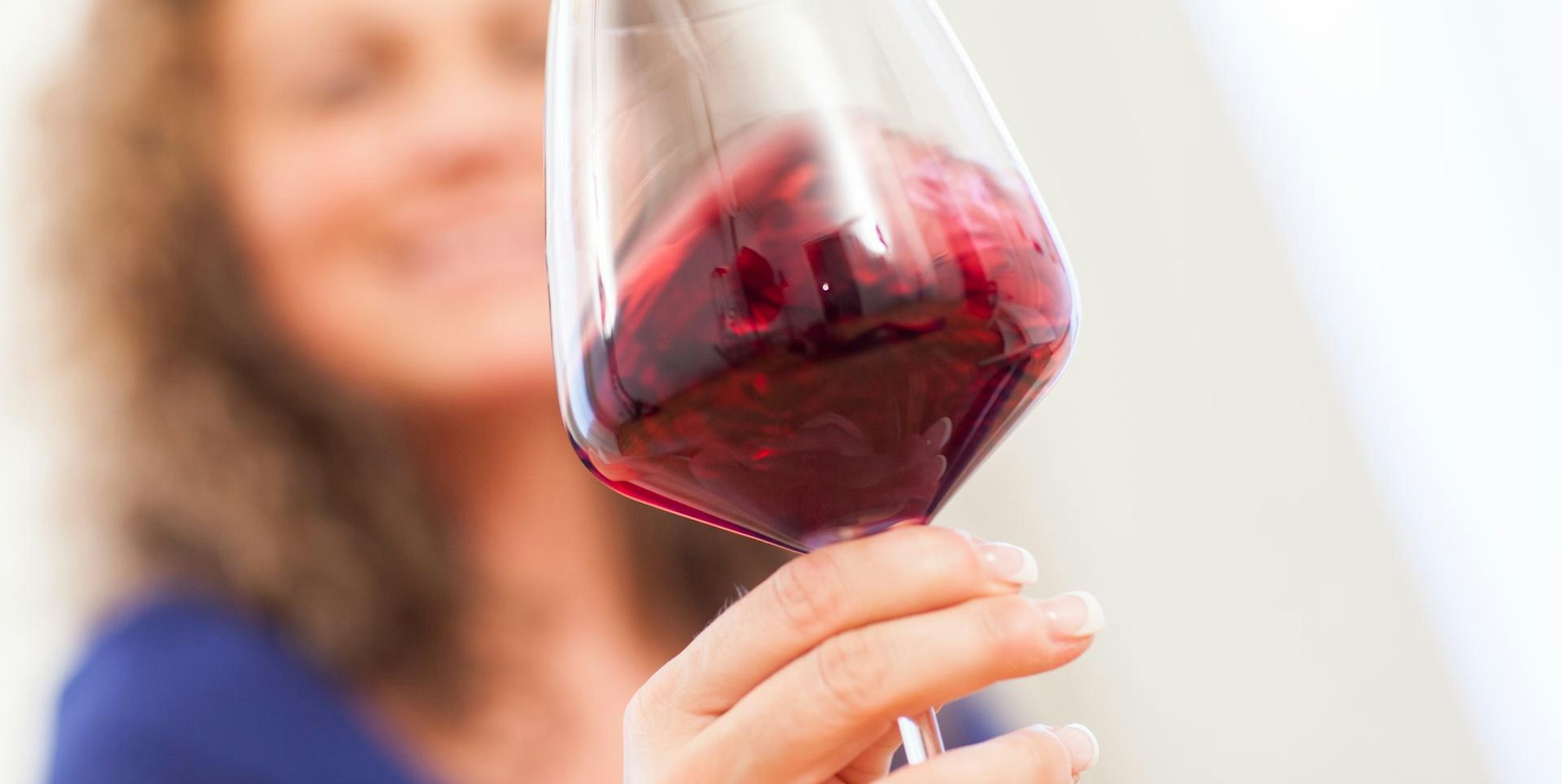 Frau hält ein Gas Rotwein in der Hand