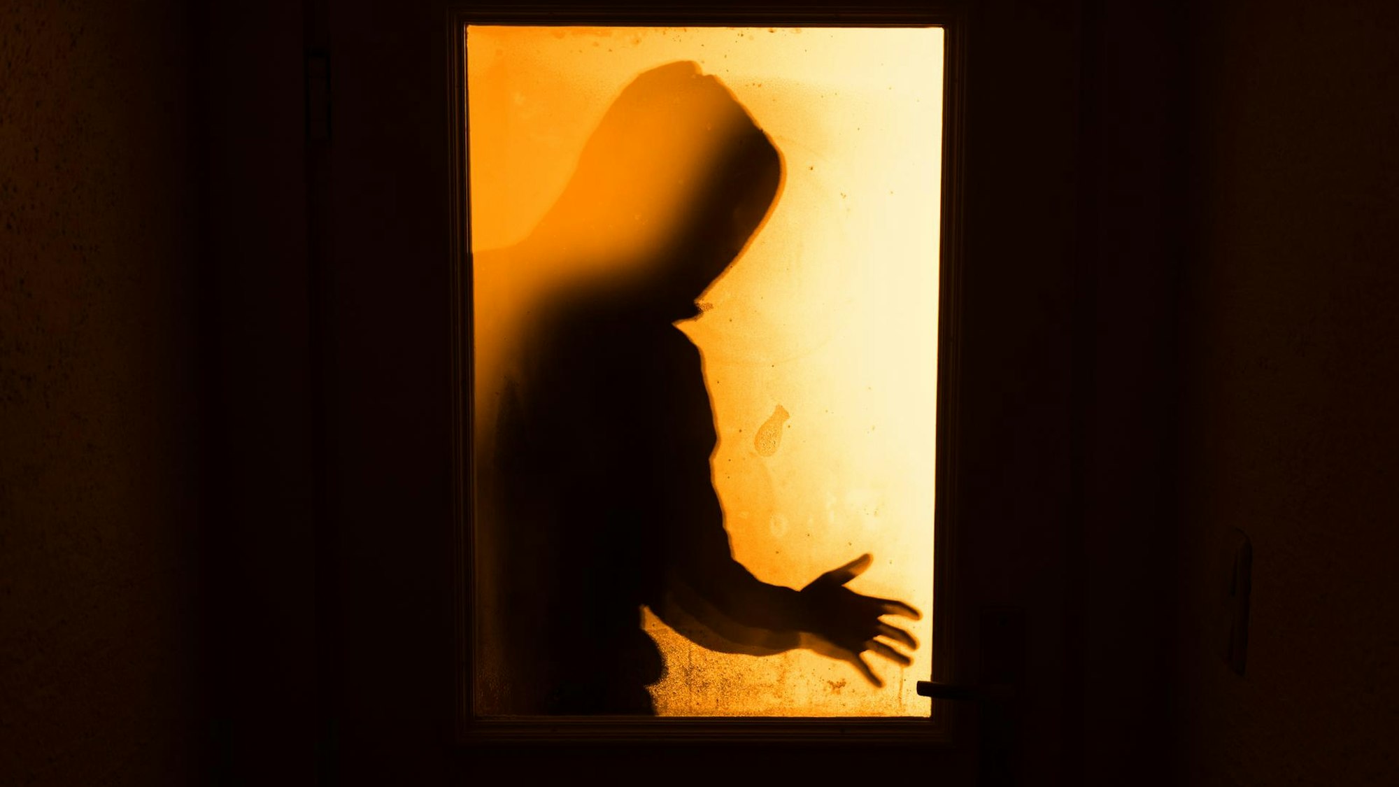 Das Bild zeigt eine Person im Gegenlicht hinter einem Fenster.