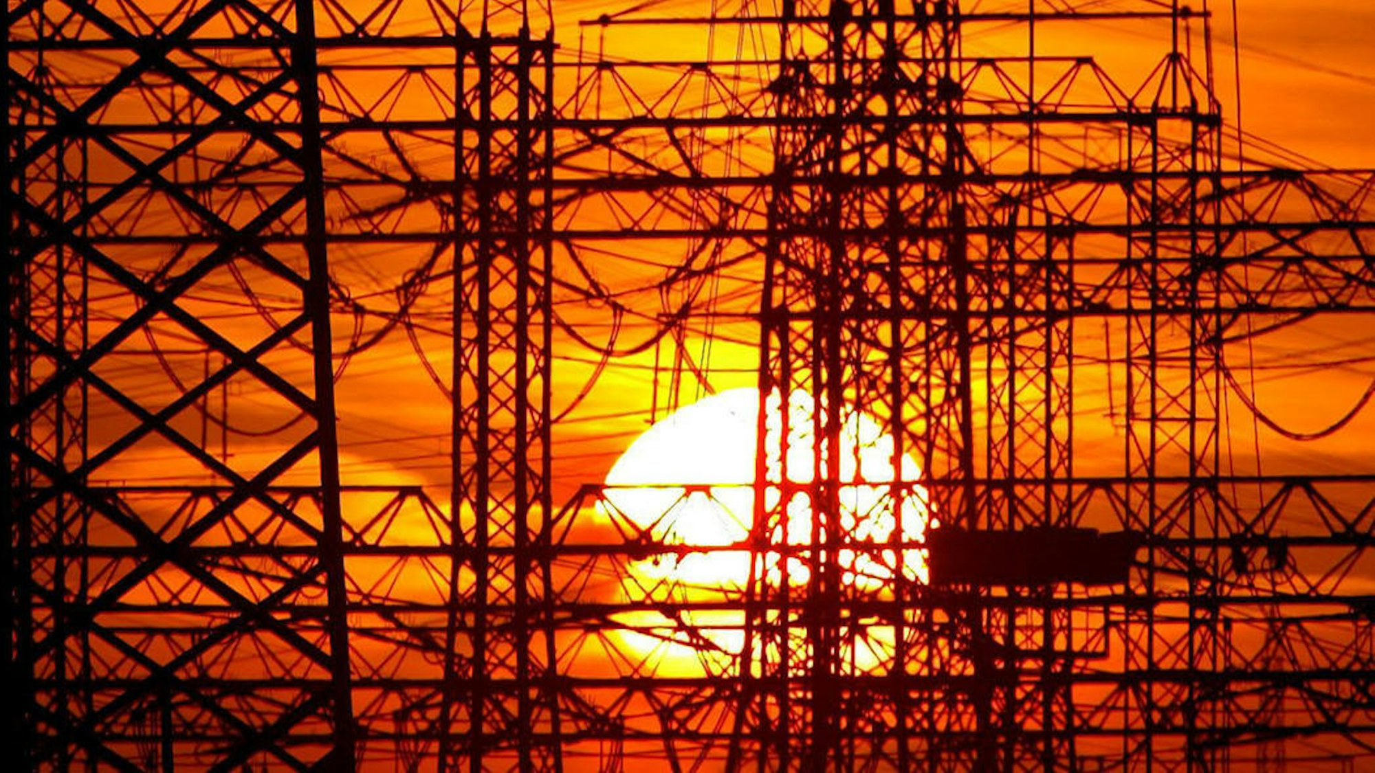 Das Bild zeigt die untergehende Sonne von zahlreichen Strommasten.