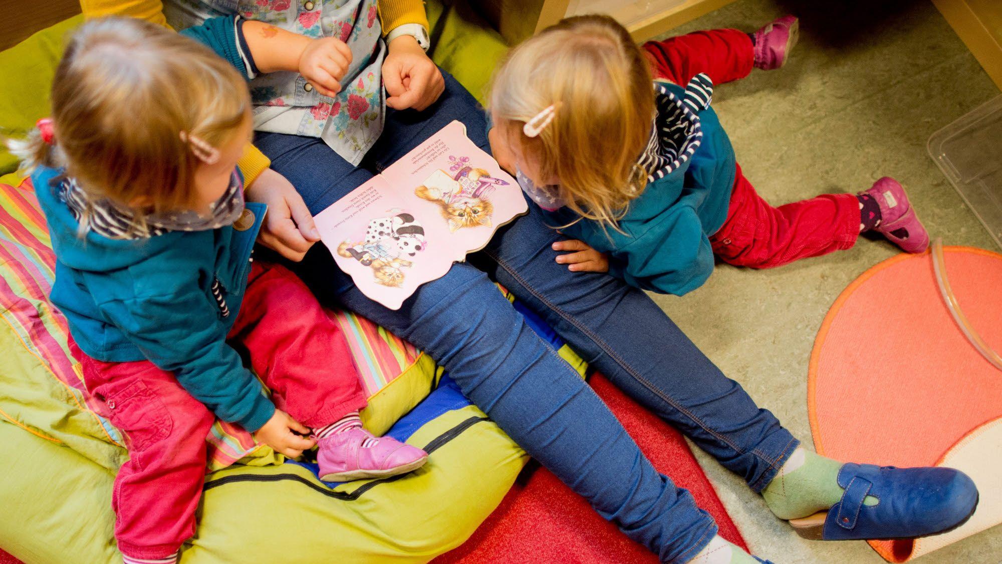 Kinder schauen in einer Kita ein Buch an