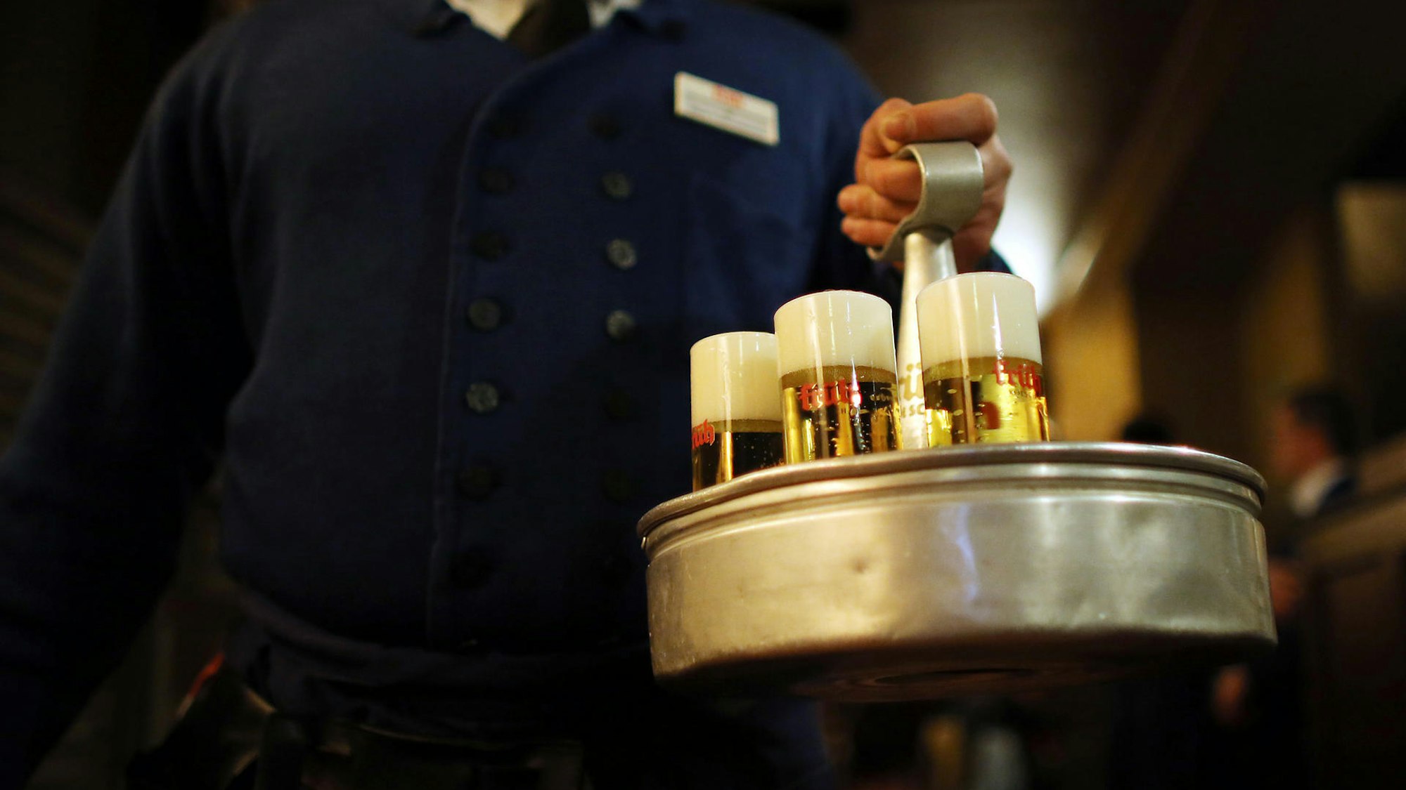 Ein Kellner trägt einen Kranz mit Kölschgläsern.