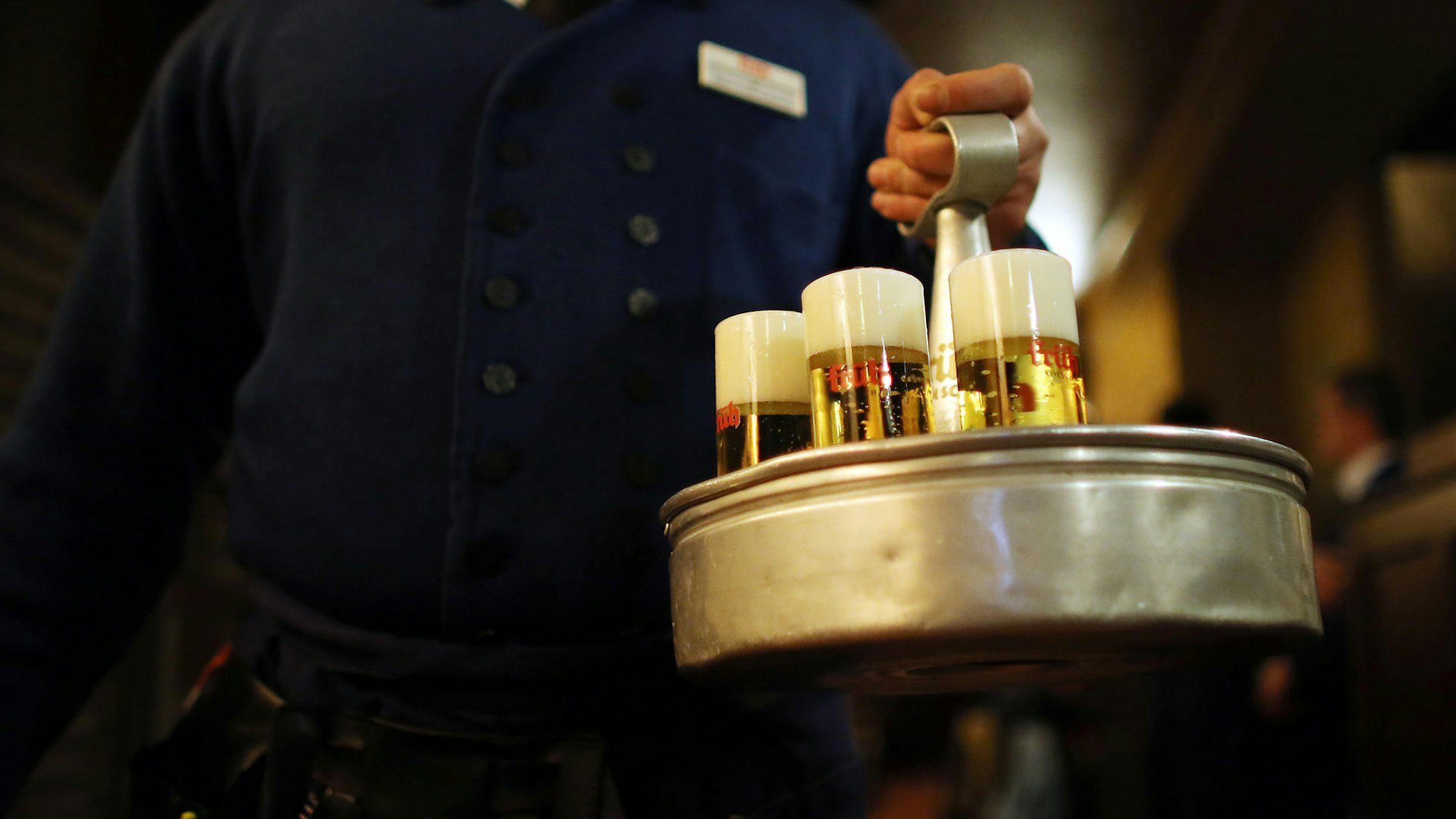 Man sieht einen Kellner, wie er Kölschgläser trägt.