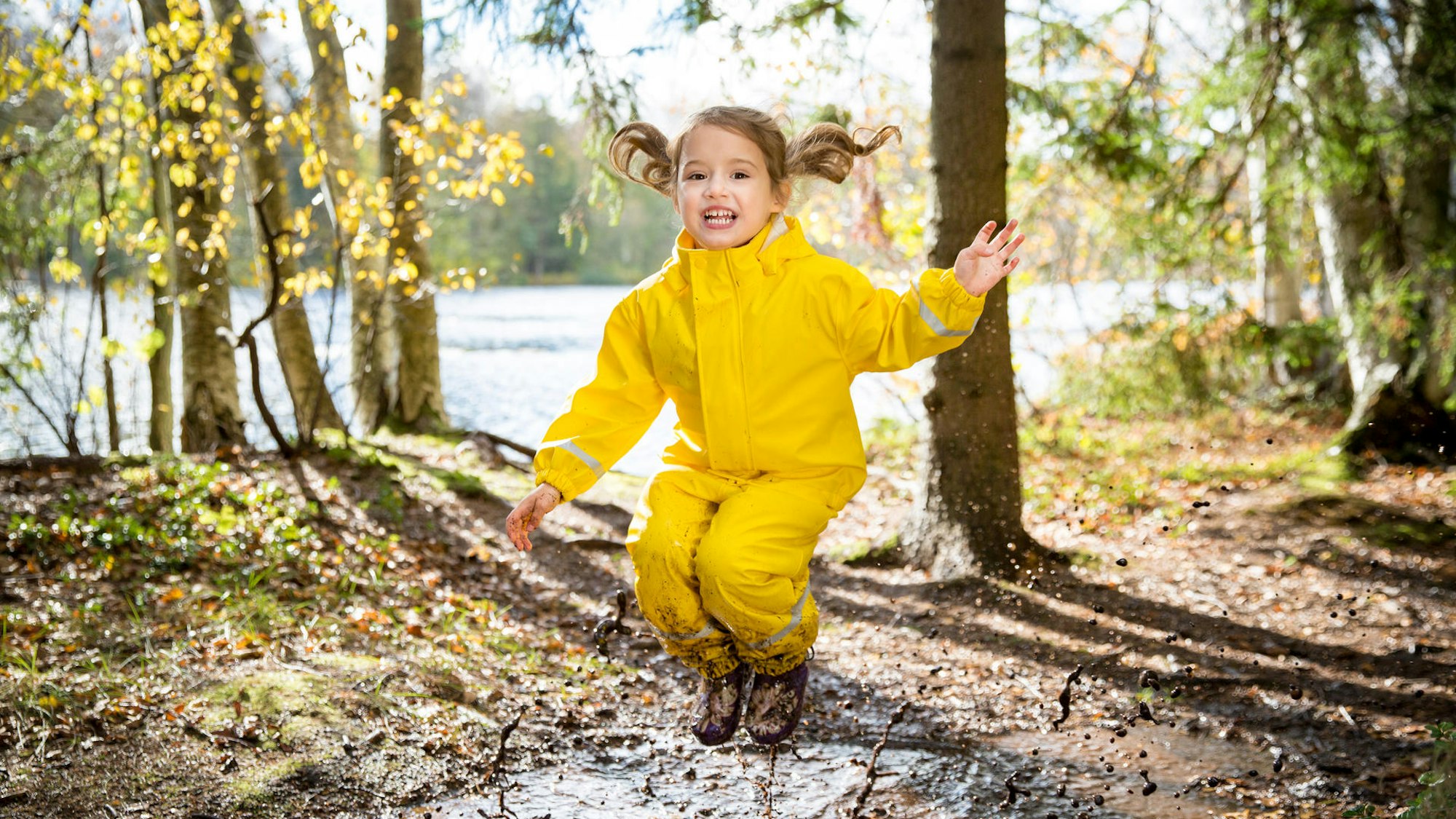 Kind in gelber Regenkleidung springt im Matsch