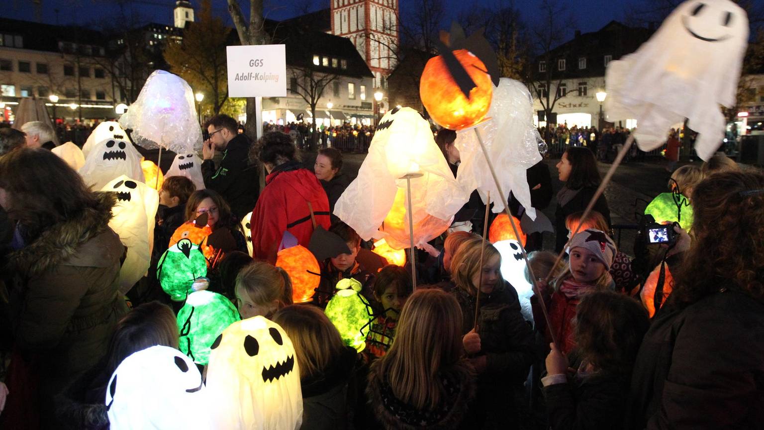Auf dem Siegburger Marktplatz stehen viele Kinder mit ihren Laternen, die aussehen wie Geister.
