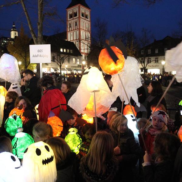 Auf dem Siegburger Marktplatz stehen viele Kinder mit ihren Laternen, die aussehen wie Geister.