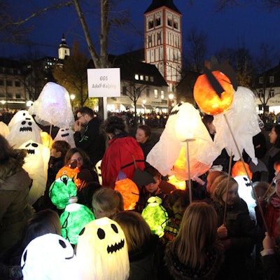 Auf dem Siegburger Marktplatz stehen viele Kinder mit ihren Laternen, die aussehen wie Geister.