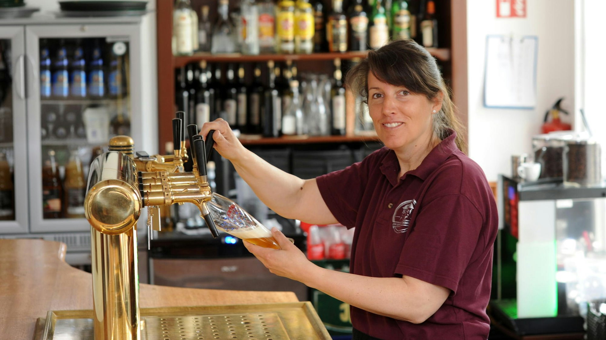 Eine Frau steht hinter der Theke am Zapfhahn und hat ein Glas in der Hand.