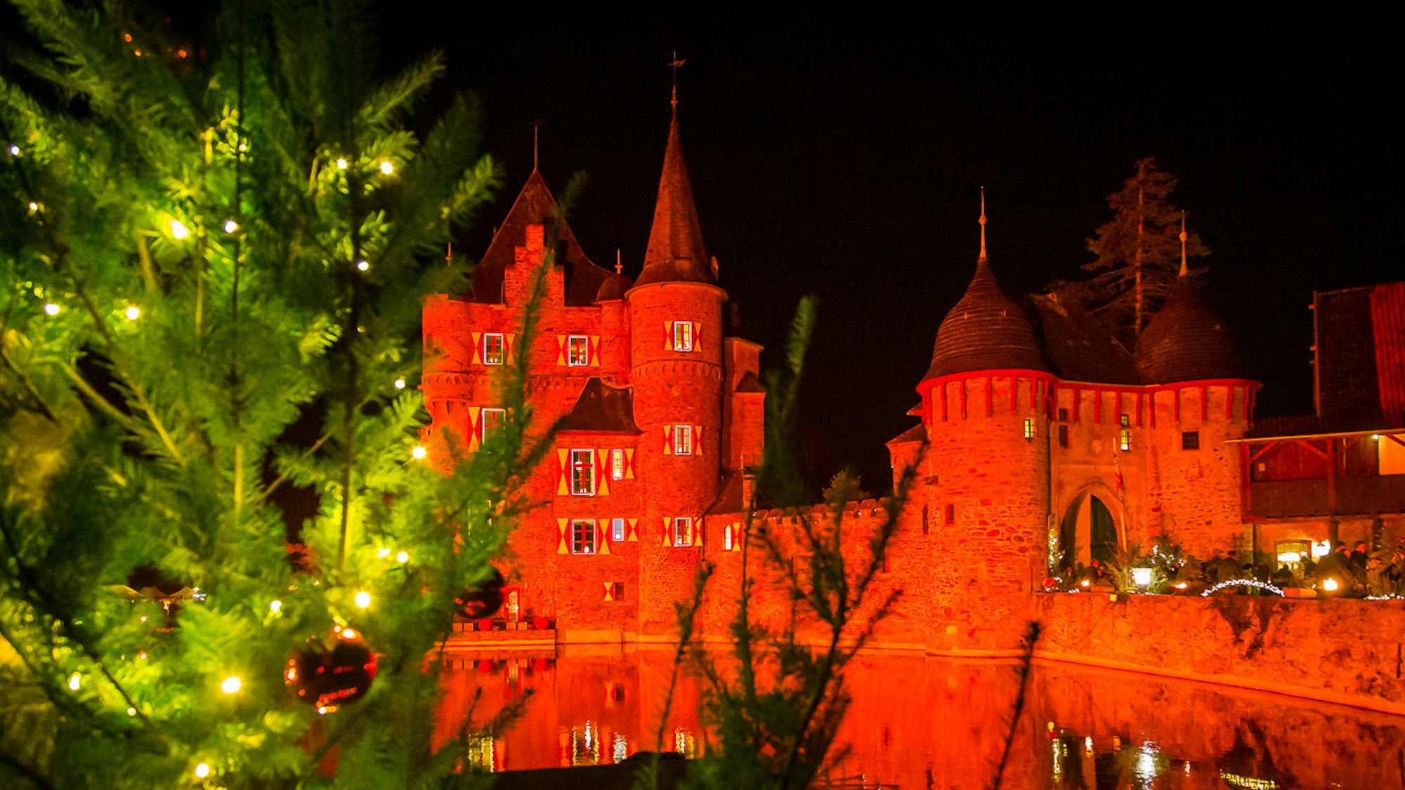 Rot angestrahlte Burg Satzvey mit Tannenbaum im Vordergrund.