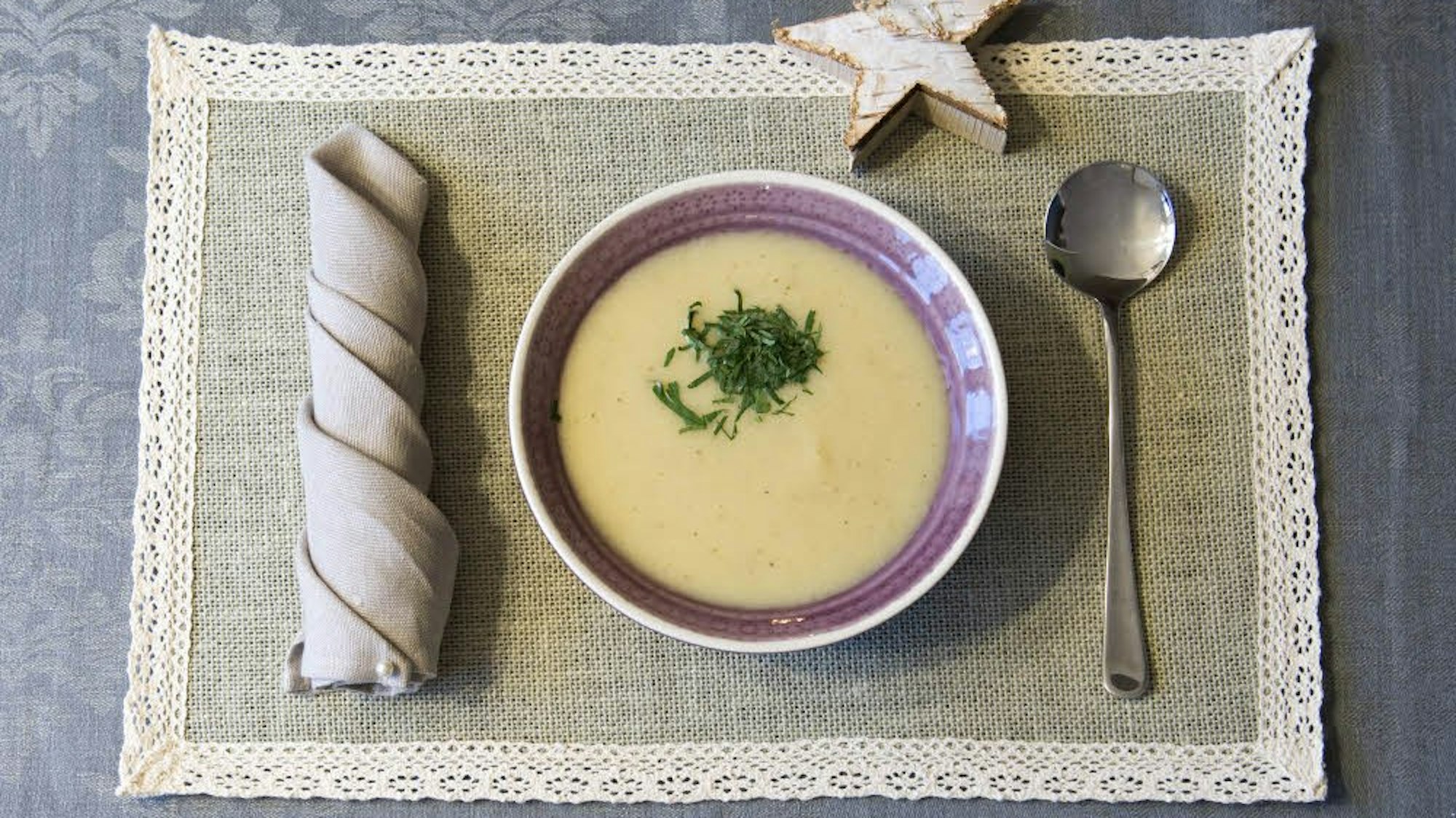 Pastinakensuppe lecker angerichtet in einer Schüssel und serviert auf einem Deckchen mit Besteck und einem Deko-Stern.