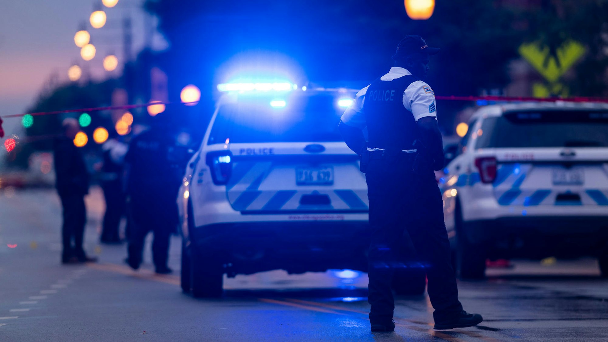Polizisten sichern eine Straße mit Einsatzfahrzeugen und Blaulicht bei Nacht.