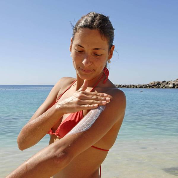 Frau cremt sich am Strand mit Sonnencreme ein