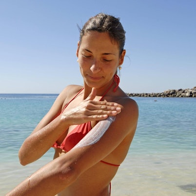 Frau cremt sich am Strand mit Sonnencreme ein