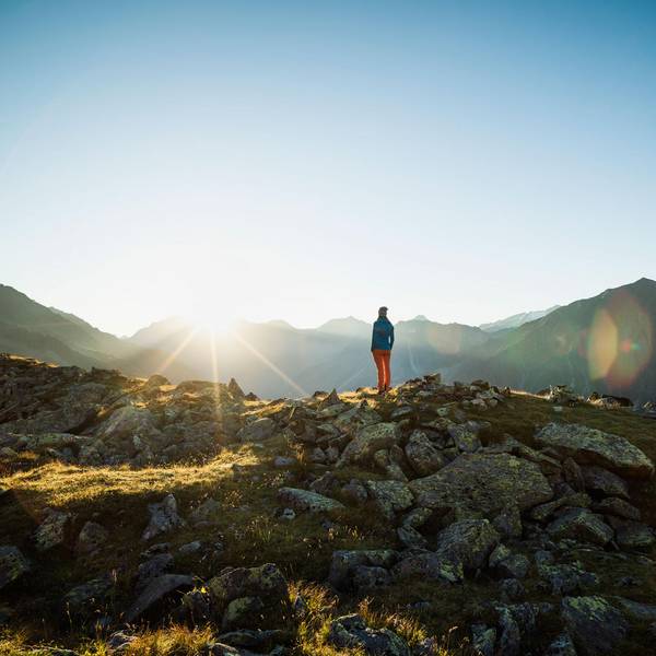 Eine Frau steht in einer Berglandschaft und schaut in die Weite.