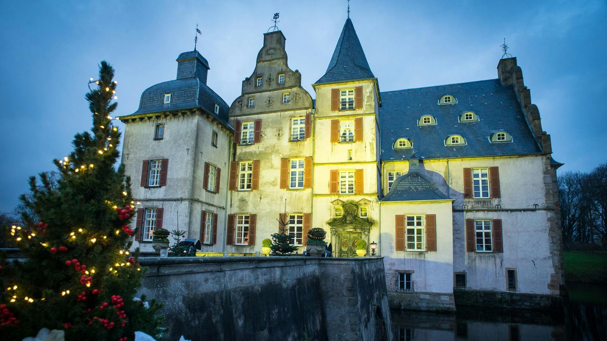 Beleuchtetes Wasserschloss Bodelschwingh mit Tannenbaum im Vordergrund.