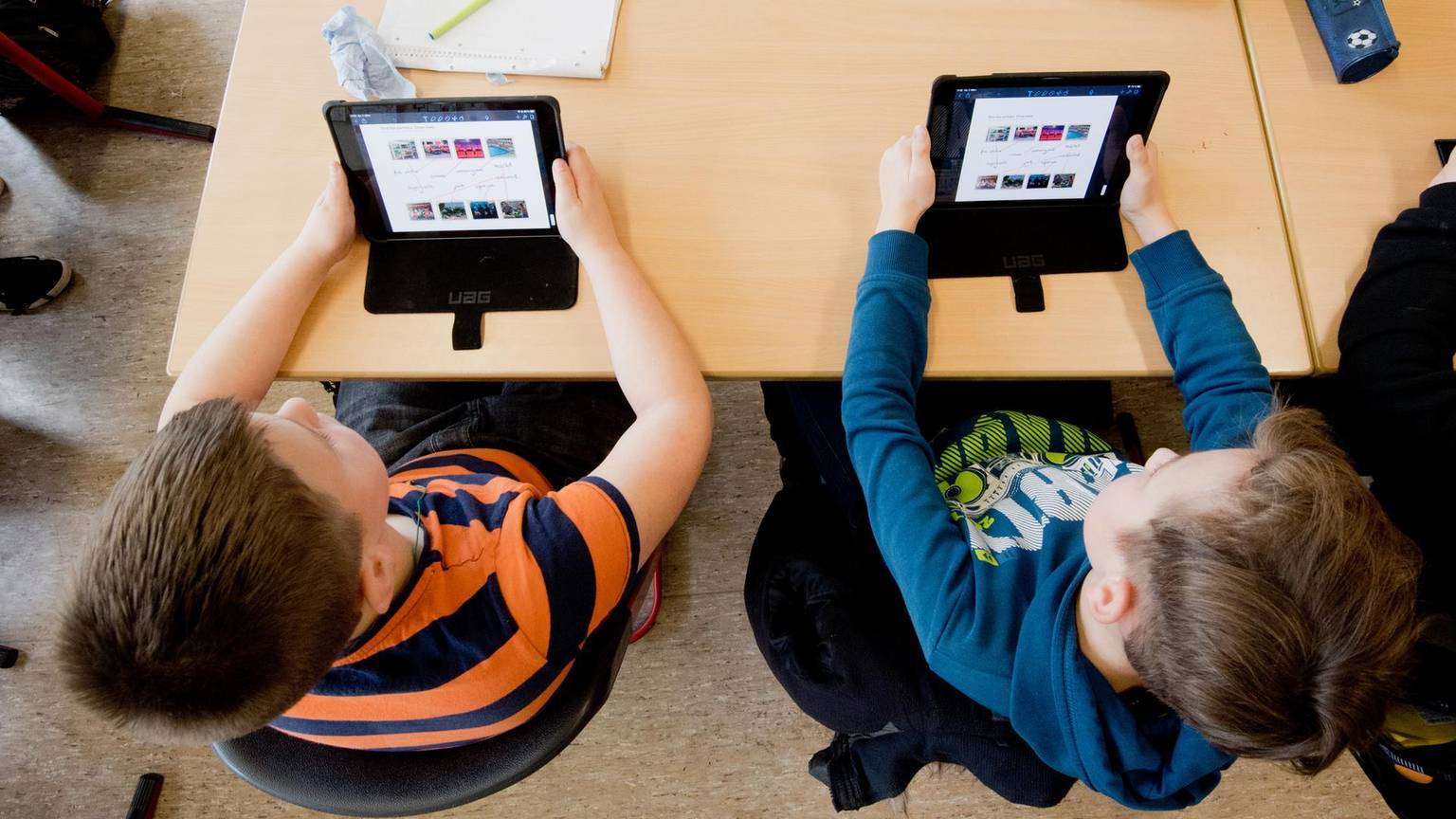 Zwei Jungen sitzen an einem Schulpult und lernen auf einem Tablet.