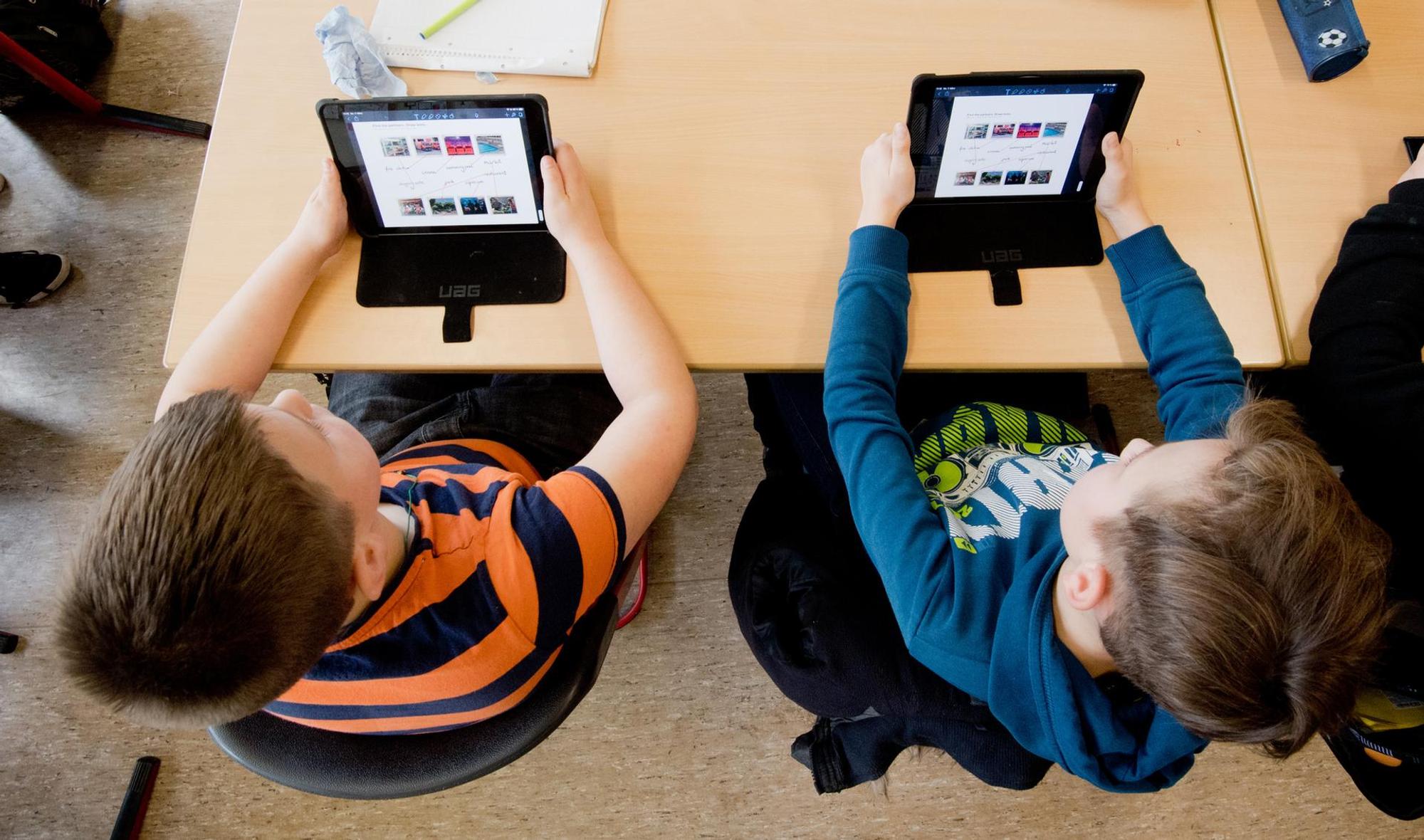 Zwei Jungen sitzen an einem Schulpult und lernen auf einem Tablet.