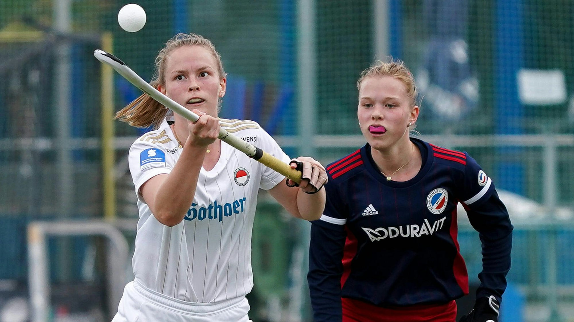Eine Hockeyspielerin balanciert den Ball auf dem Schläger, ihre Gegnerin schaut zu.