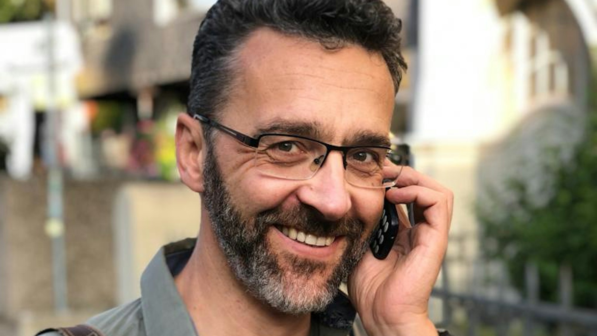 Axel Gerschlauer hält sich ein Telefon ans Ohr, während er auf einem Weg steht und in die Kamera blickt.