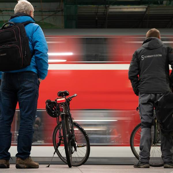 Menschen stehen an einem Bahnsteig, während ein roter Regionalzug einfährt.