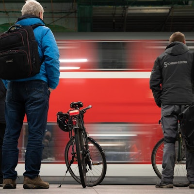 Menschen stehen an einem Bahnsteig, während ein roter Regionalzug einfährt.