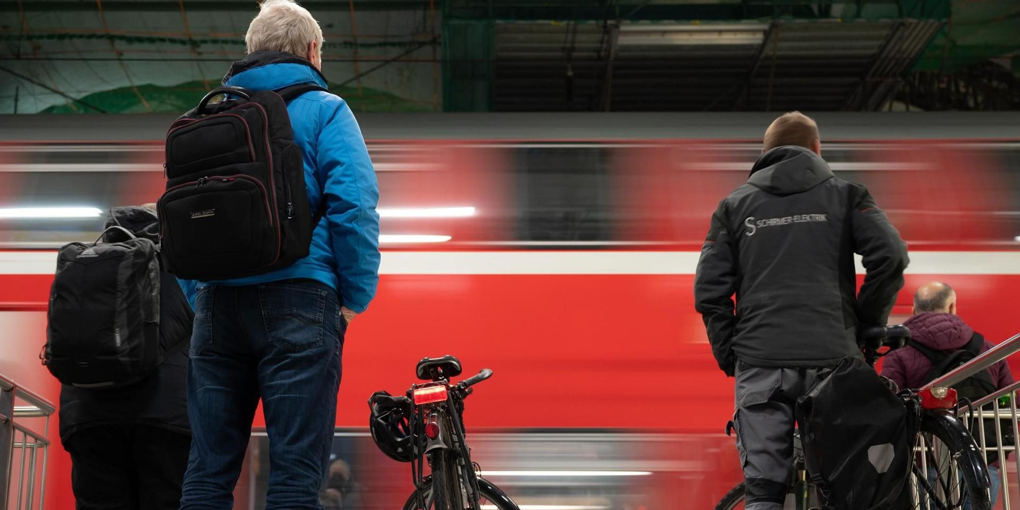 Menschen stehen an einem Bahnsteig, während ein roter Regionalzug einfährt.