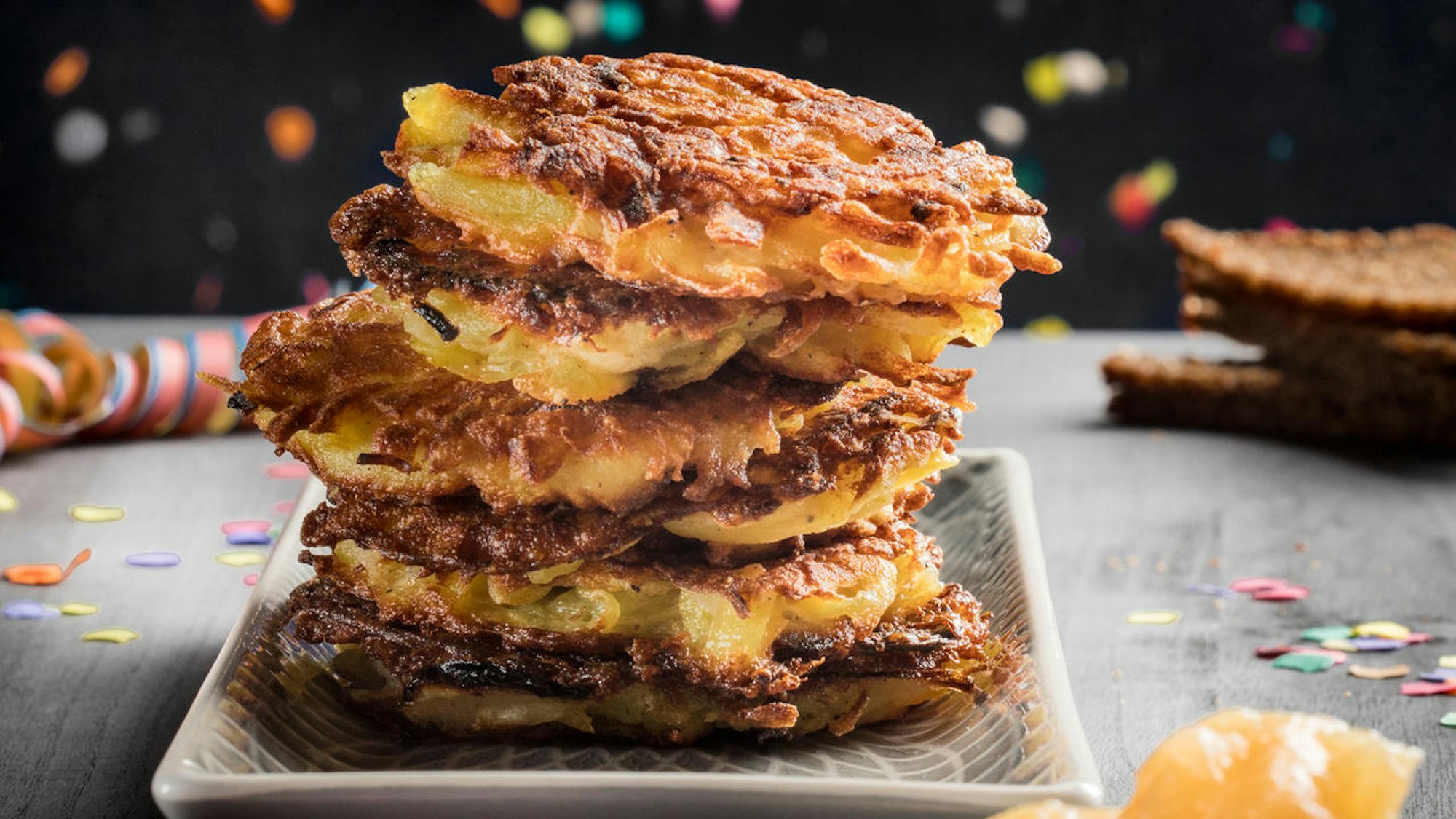 Reibekuchen liegen aufeinandergestapelt auf einem Teller, im Hintergrund sind bunte Luftschlangen zu erkennen