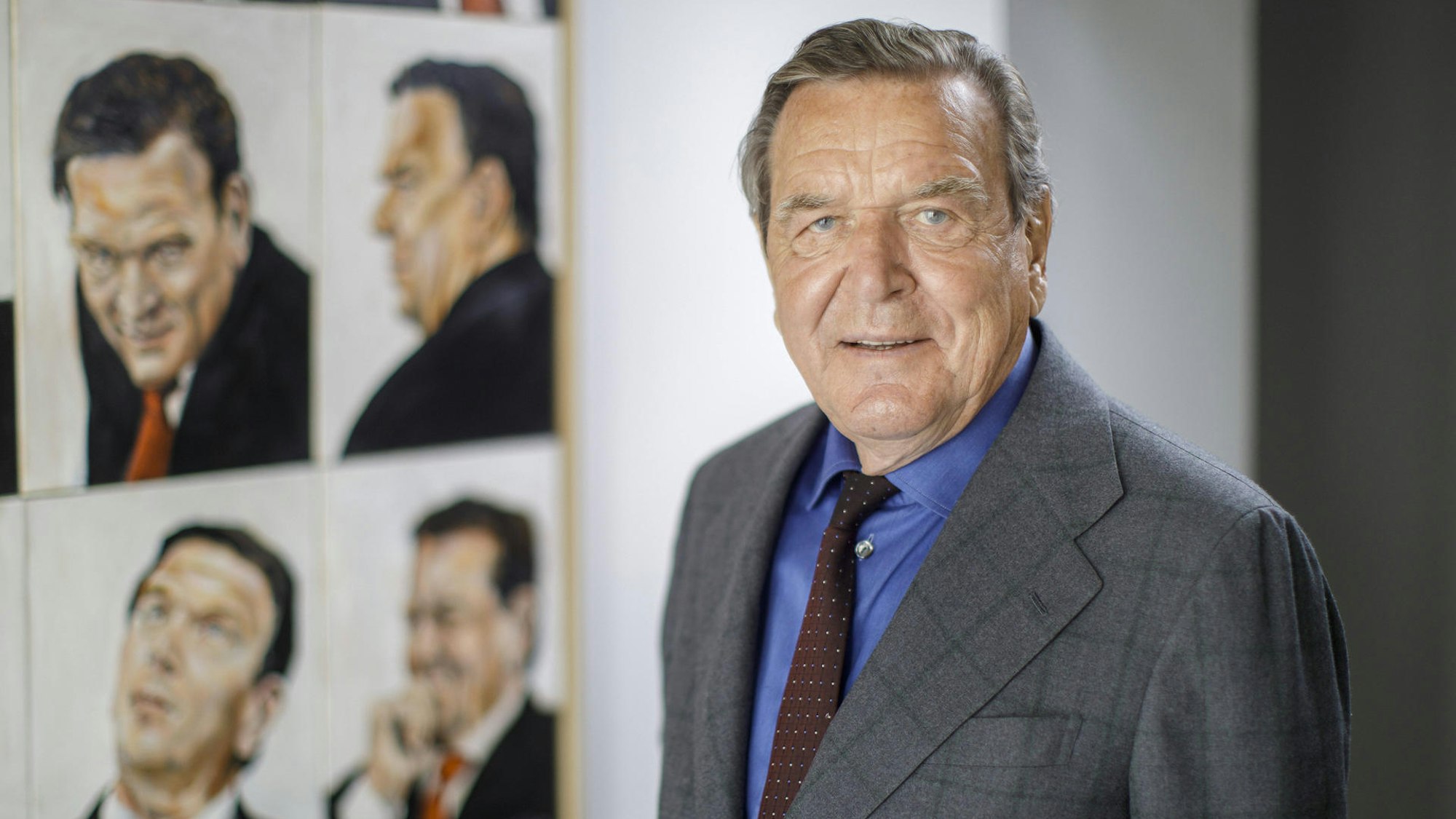 Gerhard Schröder steht vor gemalten Porträts von sich.