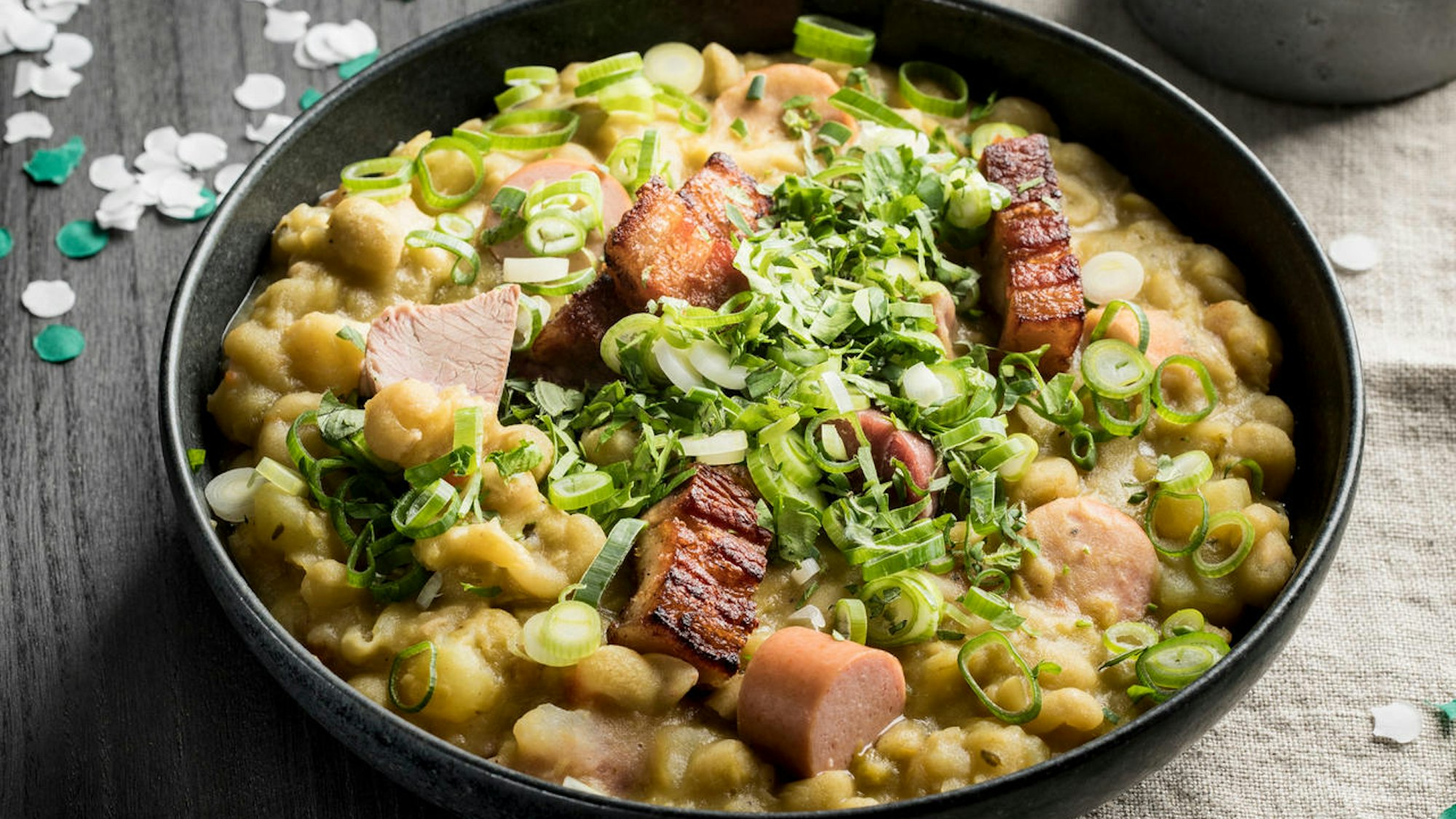 Erbsensuppe mit Wurst, angerichtet in einer Schale, daneben liegt Konfetti auf dem Tisch