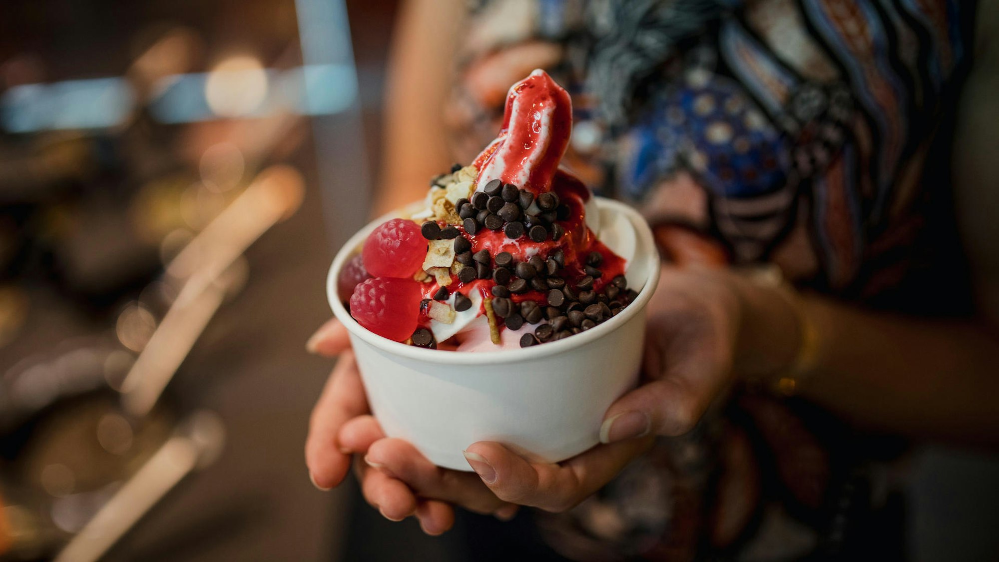 Eine Person hält einen Becher Frozen Yogurt mit Toppings in den Händen.